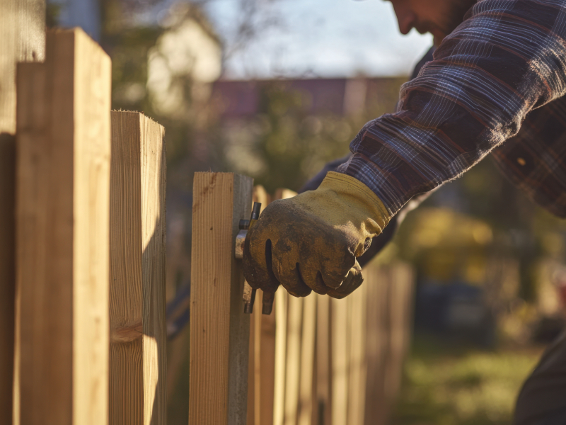 A contractor wearing work gloves aligning a new wooden picket during a residential fence installation.