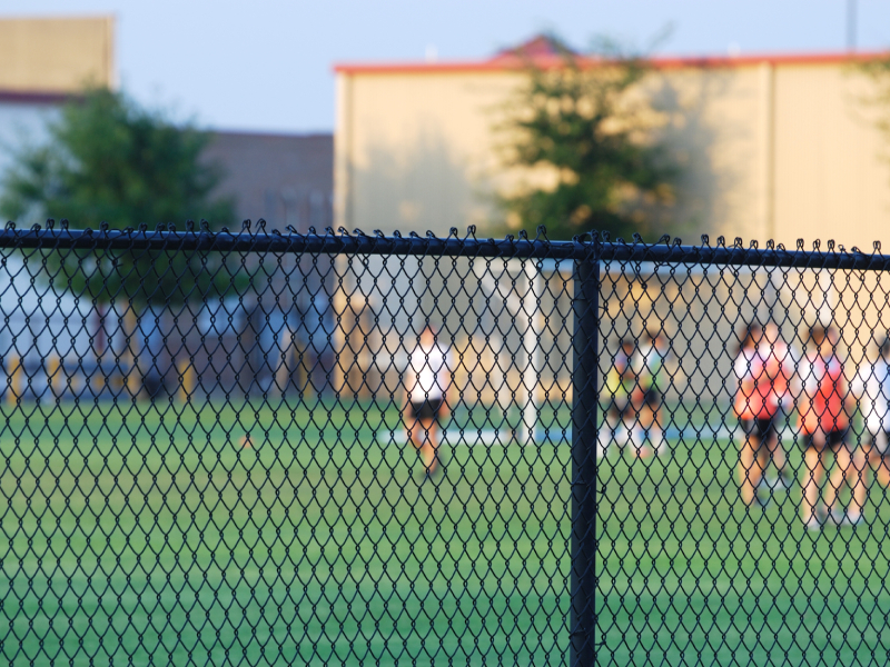 Black cyclone chain-link fencing installed outdoors in a commercial or athletic property.
