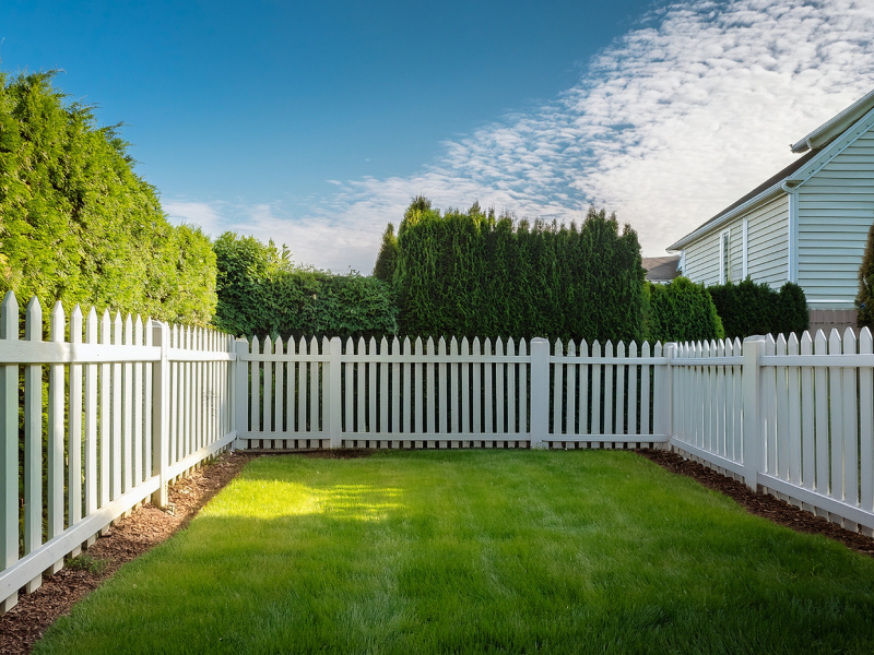 White vinyl privacy fencing installed around a residential backyard lawn in a neighborhood.