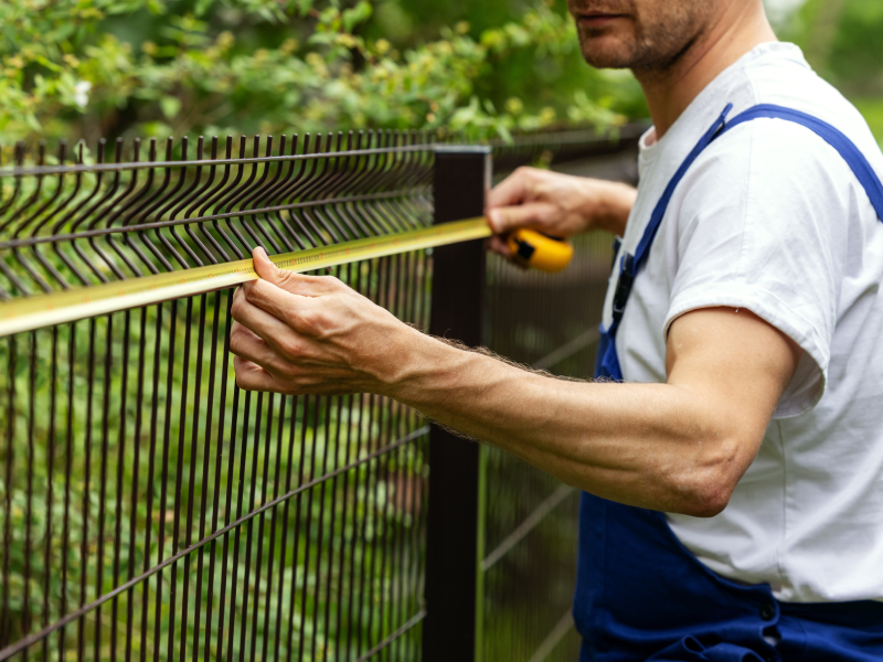 Professional fence installer measuring height along a metal wire mesh security fence during a residential installation by King Fence.
